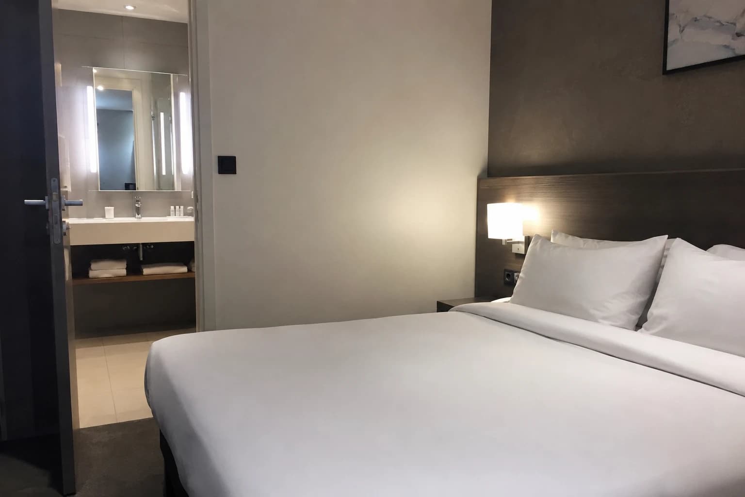 Chambre d'hôtel avec literie blanche immaculée et salle de bain impeccable, illustrant la propreté comme levier de performance hôtelière