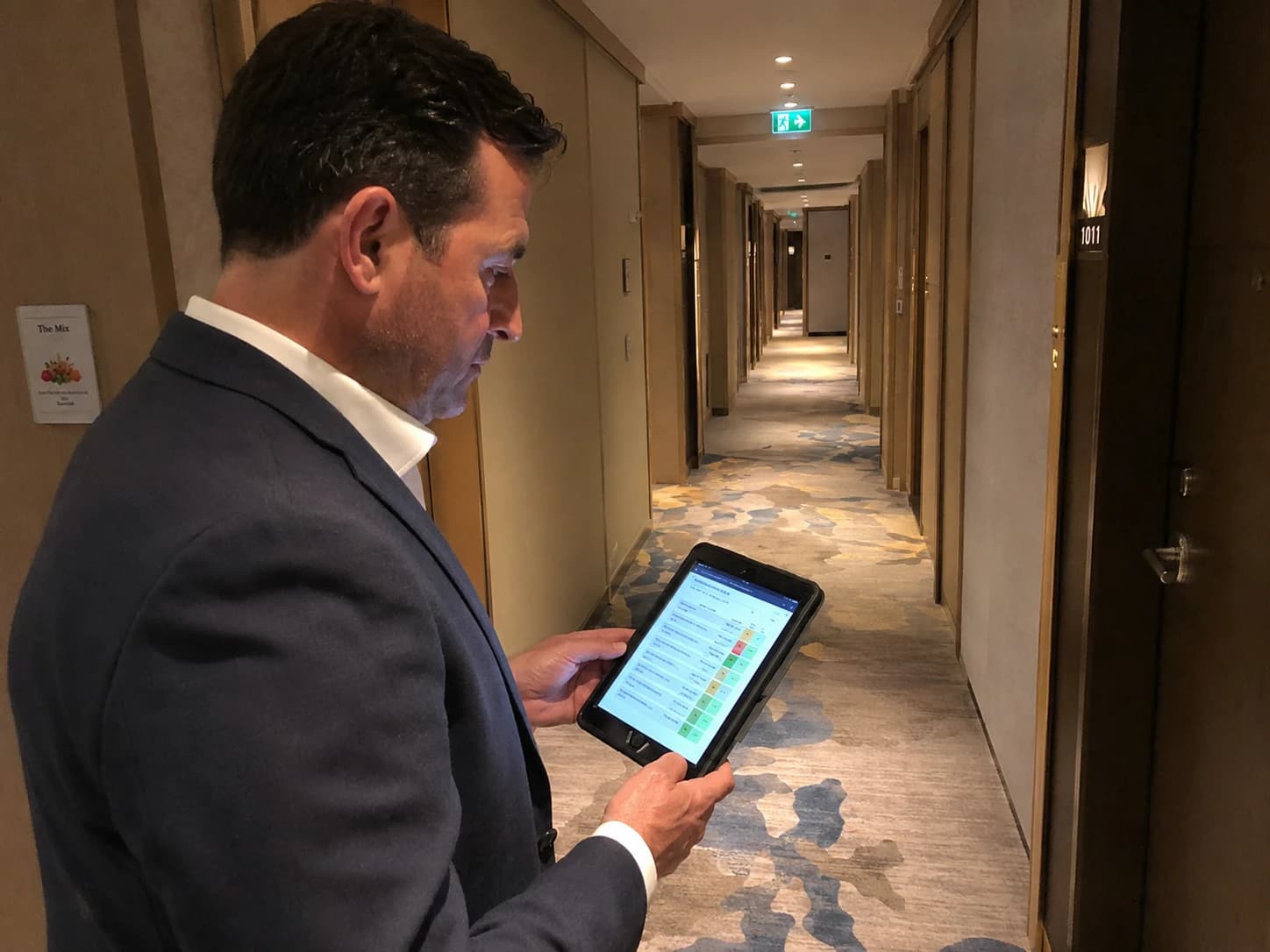 Directeur d'hôtel réalisant un auto-diagnostic propreté avec une grille d'audit sur tablette dans un couloir de chambres