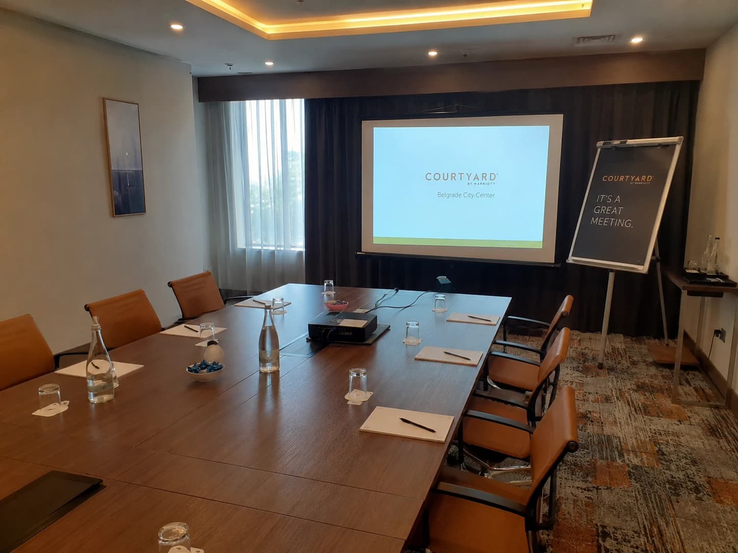 Salle de réunion d'hôtel prête pour un séminaire avec table de conférence propre, chaises alignées et équipement de présentation