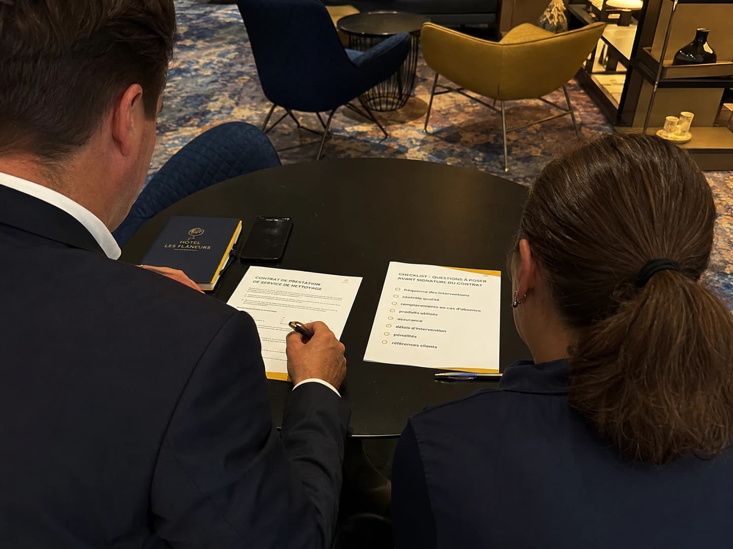 Directeur d'hôtel en réunion avec un prestataire de nettoyage, contrat sur la table avec checklist de questions a poser avant signature