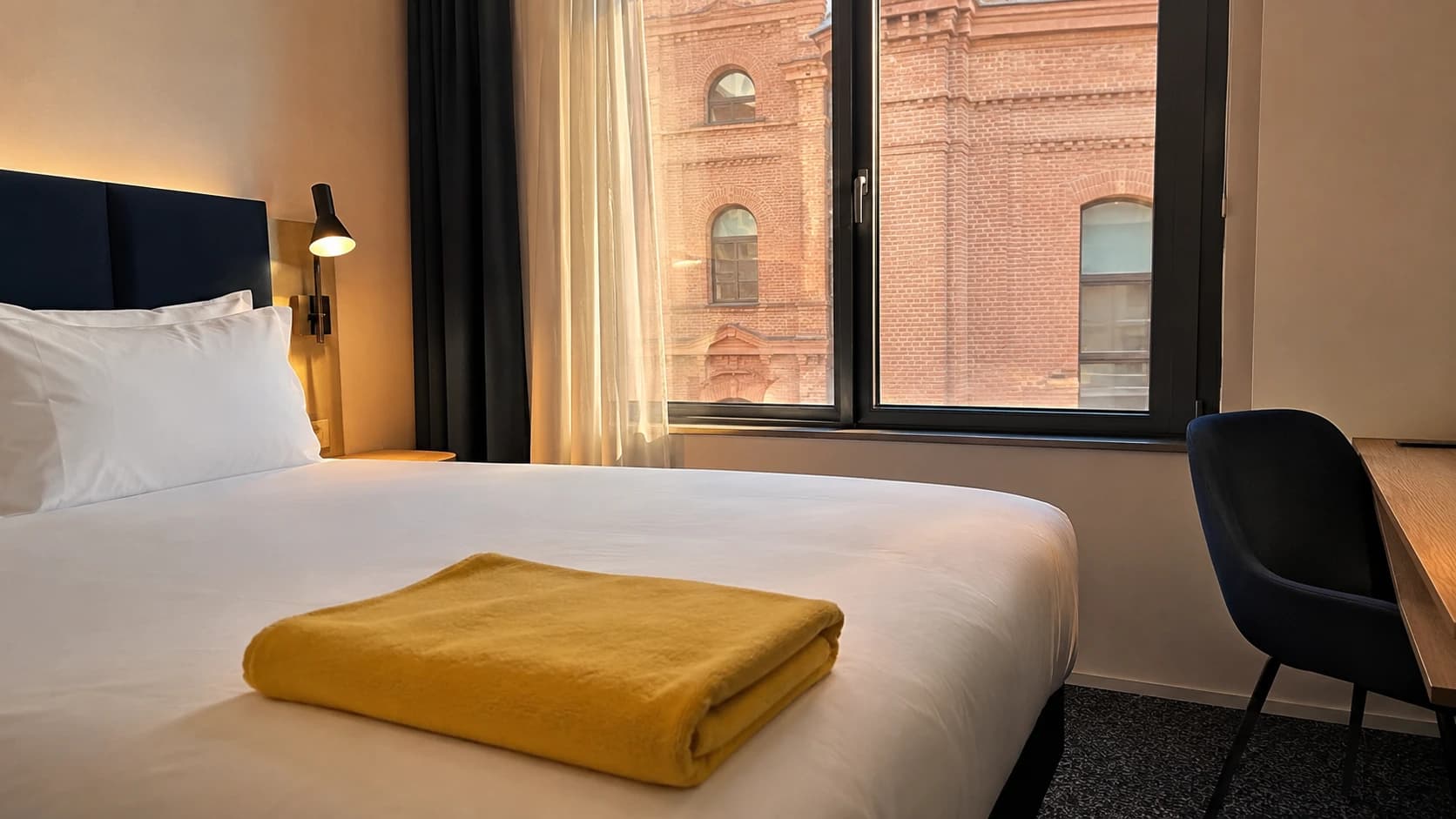 Chambre d'hôtel toulousaine aux murs de brique rose fraîchement préparée, serviette jaune pliée sur le lit, ambiance clientèle d'affaires