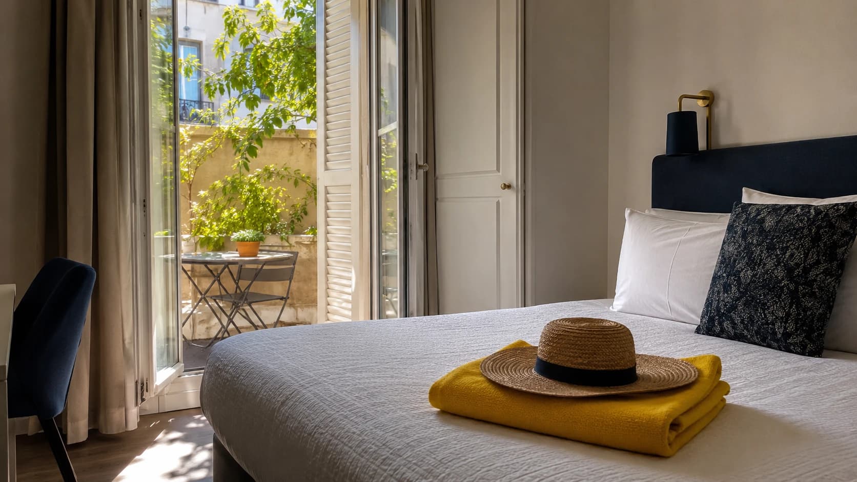 Chambre d'hôtel montpelliéraine baignée de lumière estivale avec terrasse ombragée et serviette jaune pliée, ambiance littoral méditerranéen